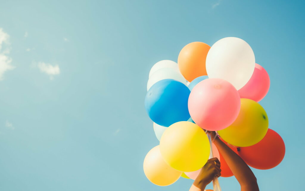 Bursting with Joy: A Vibrant Balloon Bouquet against a Blue Sky - QHD Wallpaper Delight