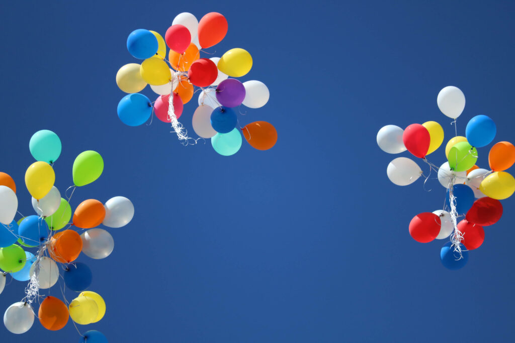 Three vibrant balloon clusters floating in clear blue sky cheerful colorful wallpaper background