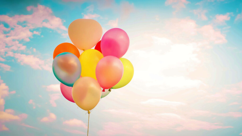 Colorful balloons floating against bright blue sky with fluffy clouds cheerful celebration background Wallpaper