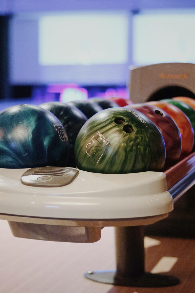 Close-up of colorful glossy bowling balls in white rack with blurred bowling alley background Wallpaper