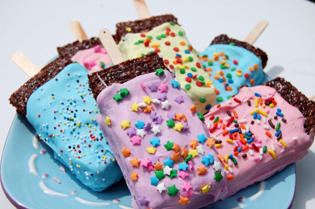 Colorful brownies on popsicle sticks with pastel icing rainbow sprinkles festive dessert background Wallpaper