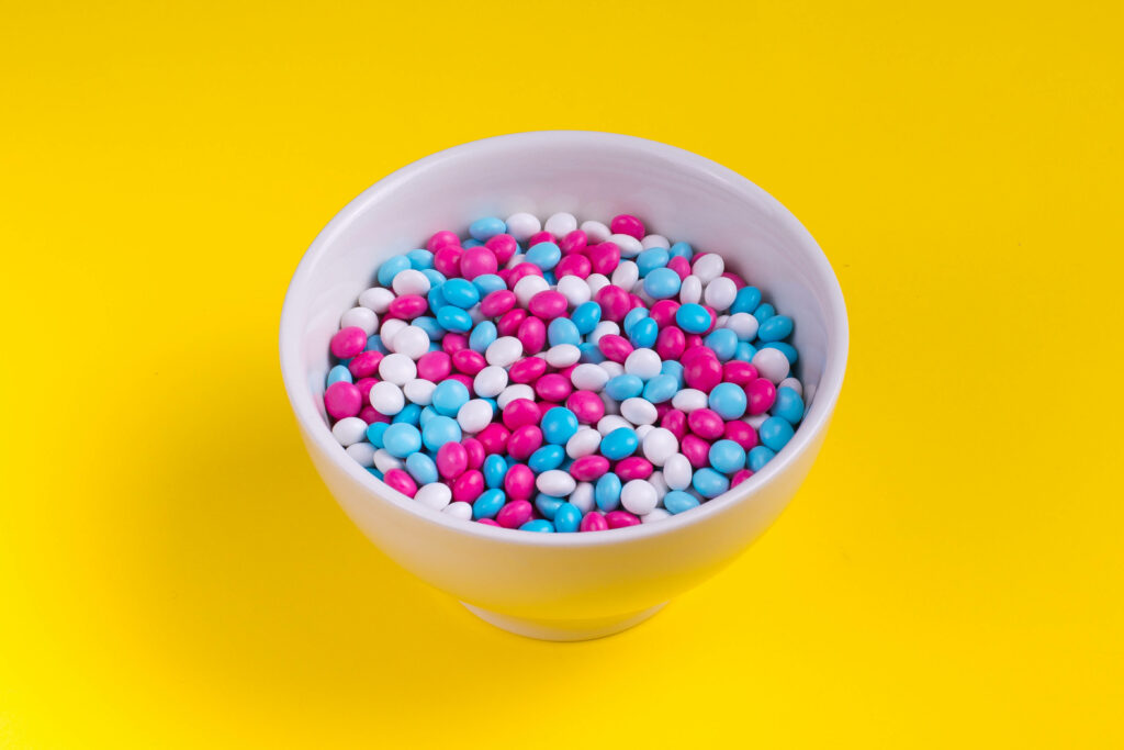Bowl of pastel pink blue and white candy-coated chocolates on bright yellow background wallpaper
