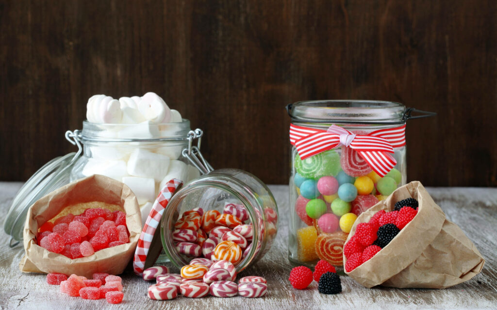 Colorful candies and marshmallows in jars and bags on rustic wooden background wallpaper