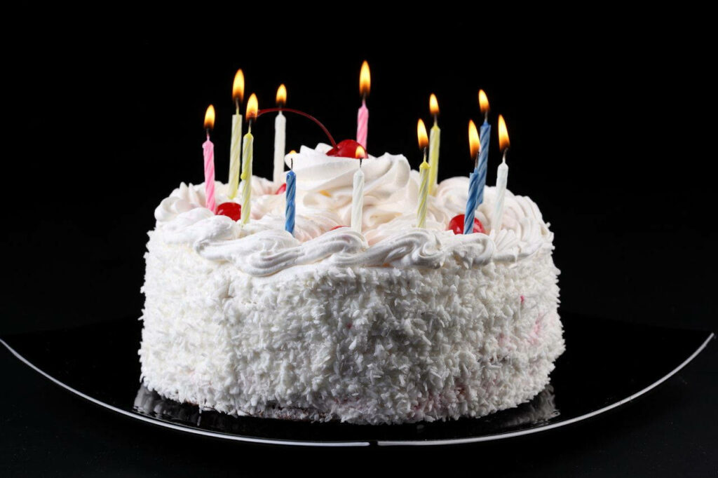 Colorful birthday cake with flickering candles and delicious coconut topping on a captivating backdrop Wallpaper