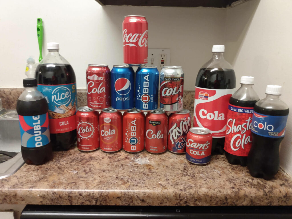 Colorful assortment of Coca-Cola Pepsi and Shasta cola cans and bottles on kitchen counter Wallpaper