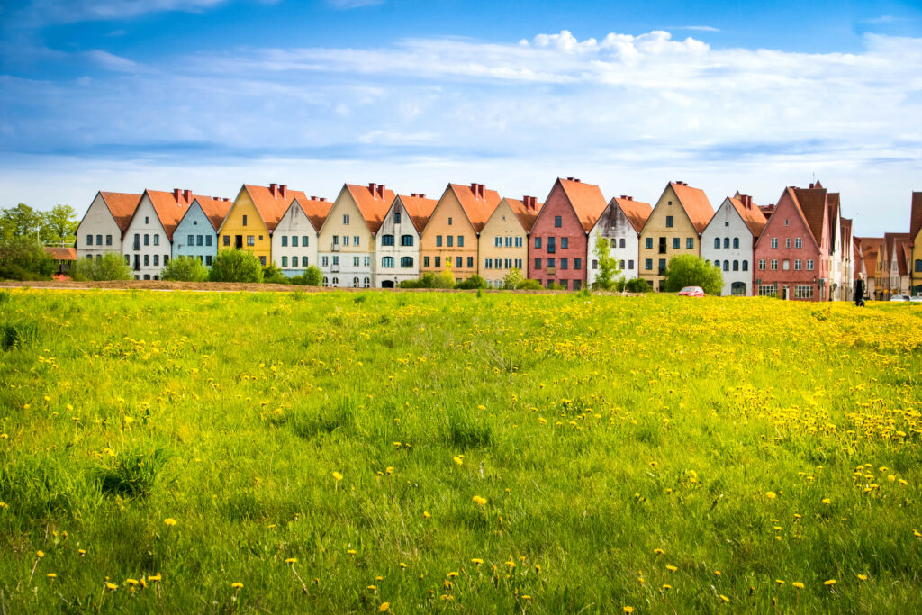Colorful cottages along green field with yellow wildflowers under sunny summer sky wallpaper