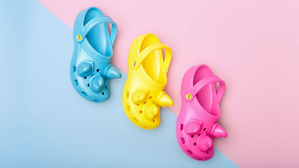 Vibrant pastel Crocs with cartoon peep charms diagonally on split pink and blue wallpaper background