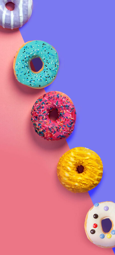 Vibrant diagonal colorful donut wallpaper with sprinkles and icing on pink and purple background