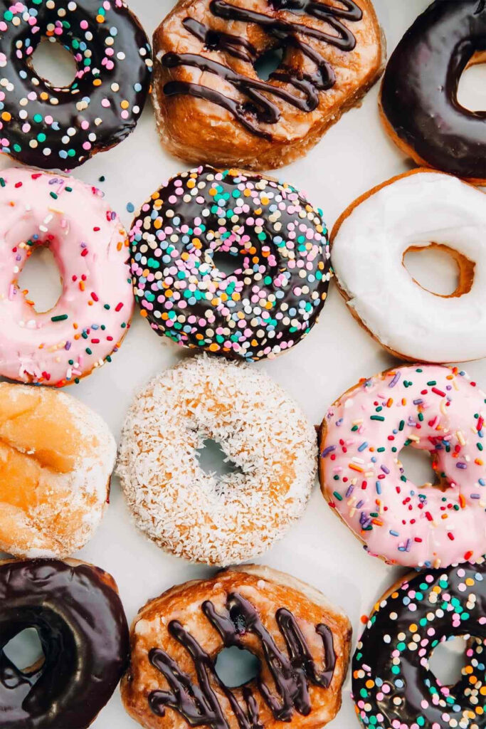 Colorful assortment of glossy donuts with chocolate vanilla pink icing and rainbow sprinkles wallpaper