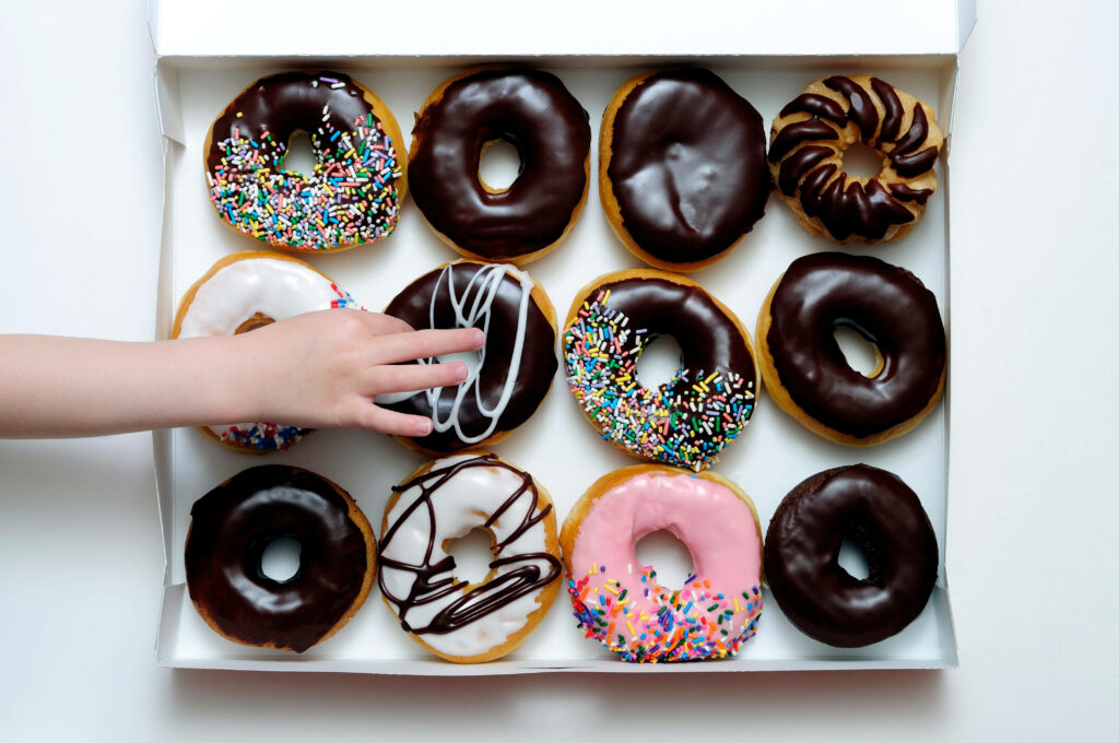 Colorful assorted donuts with sprinkles and icing in box with child’s hand reaching for one Wallpaper