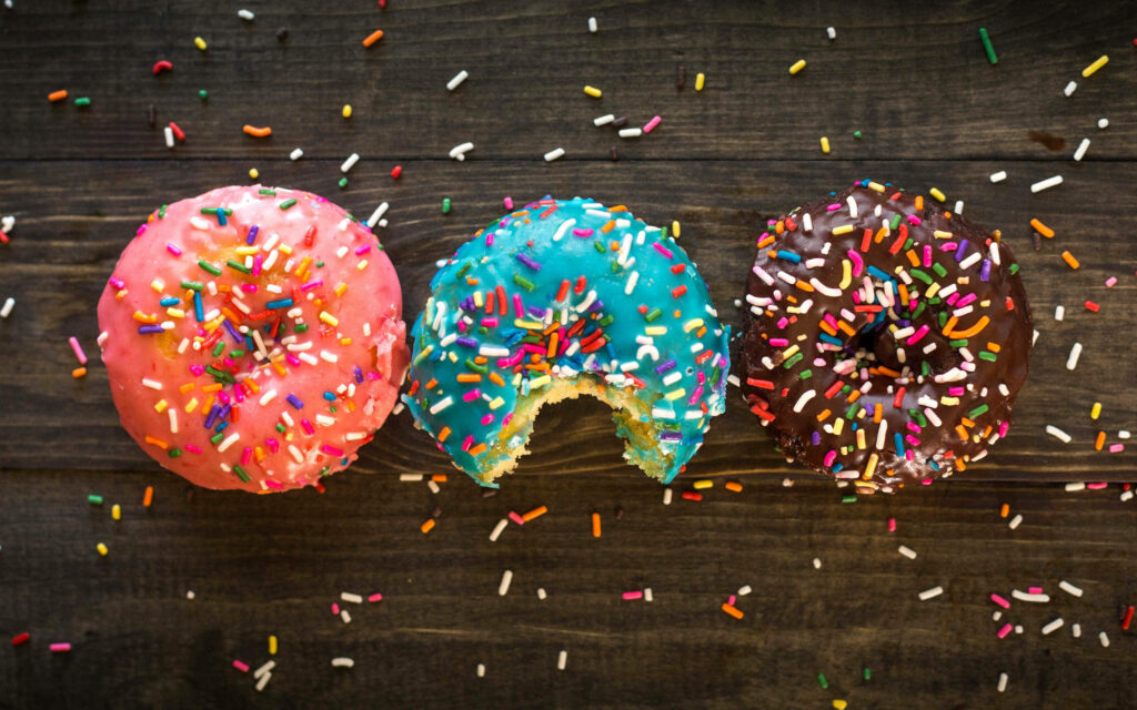 Colorful donuts with rainbow sprinkles on rustic wood background with playful bite on blue donut Wallpaper
