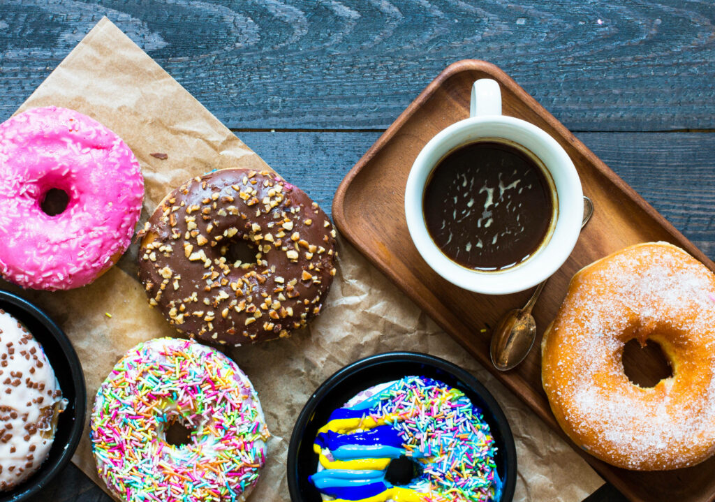 Colorful assorted donuts with sprinkles chocolate and nuts on rustic wood with coffee cup Wallpaper