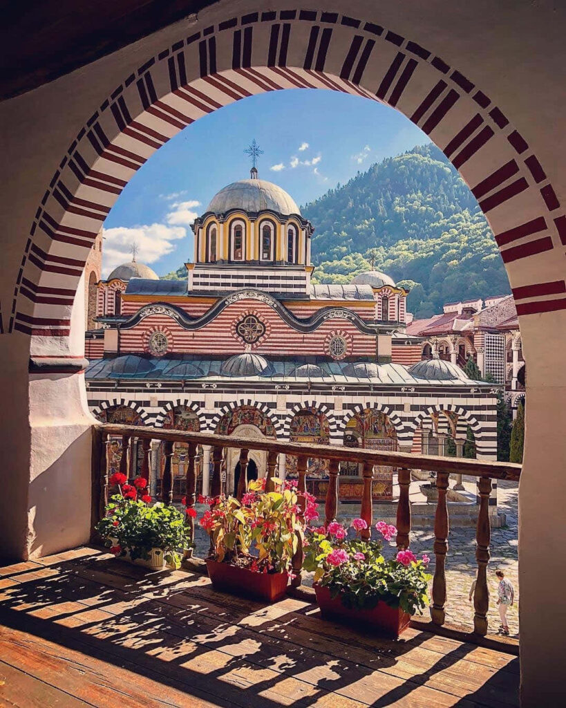 Colorful flowers on balcony with Rila Monastery and Bulgarian mountains in scenic wallpaper background