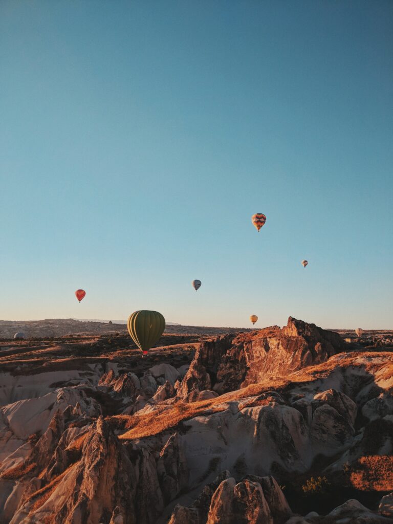 Colorful hot air balloons float over rocky mountains under clear blue sky in Turkey landscape Wallpaper