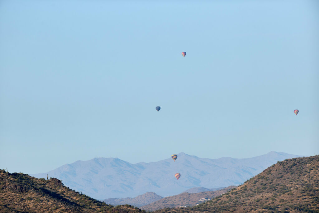 Colorful hot air balloons float over rugged mountains under clear blue sky scenic adventure background Wallpaper