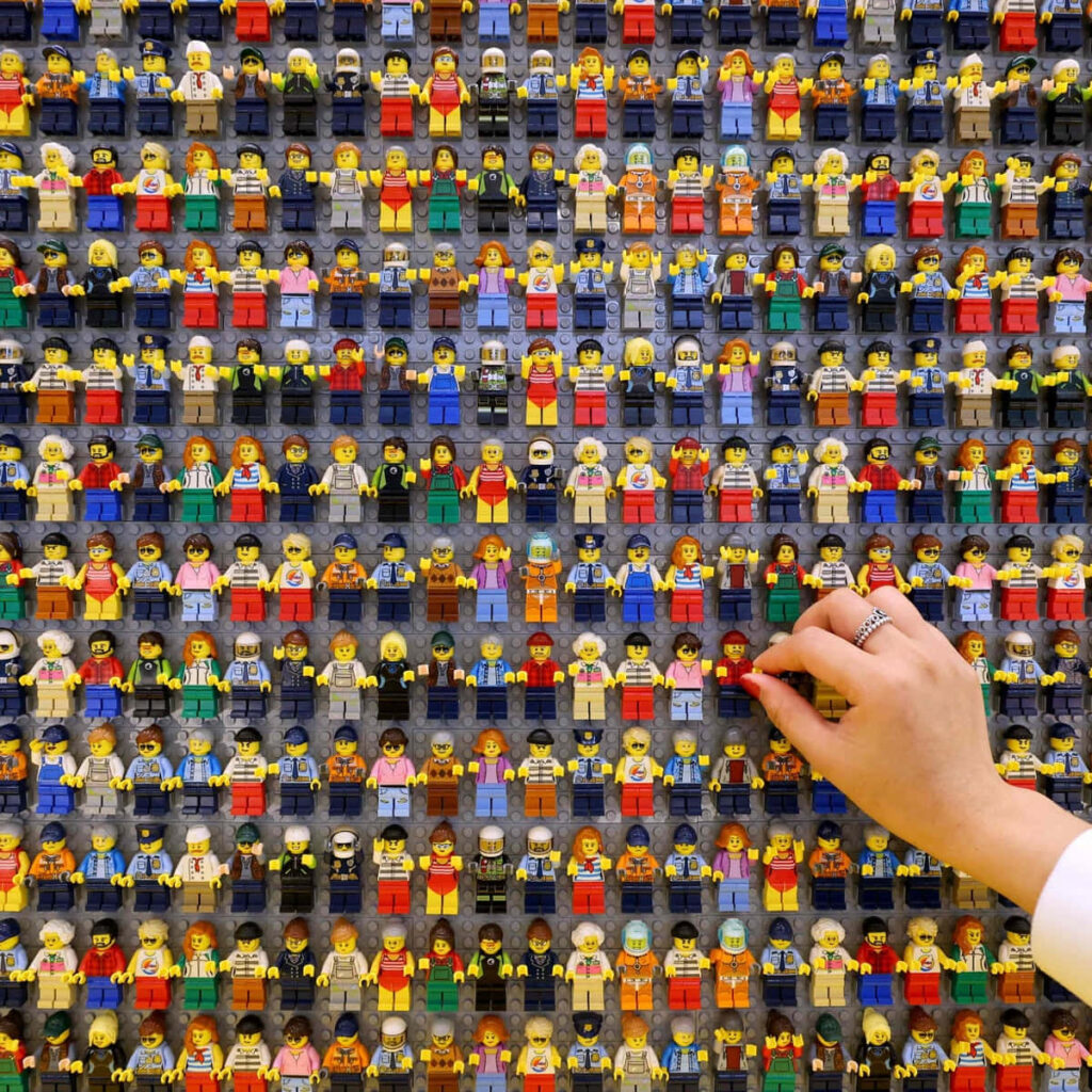 Colorful Lego minifigures displayed on wall with hand selecting figure showcasing creativity Wallpaper