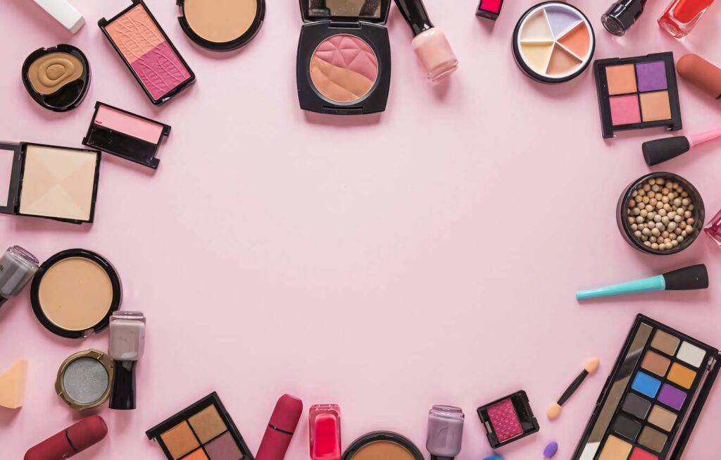Colorful makeup products including lipsticks eyeshadow palettes brushes on soft pink background Wallpaper