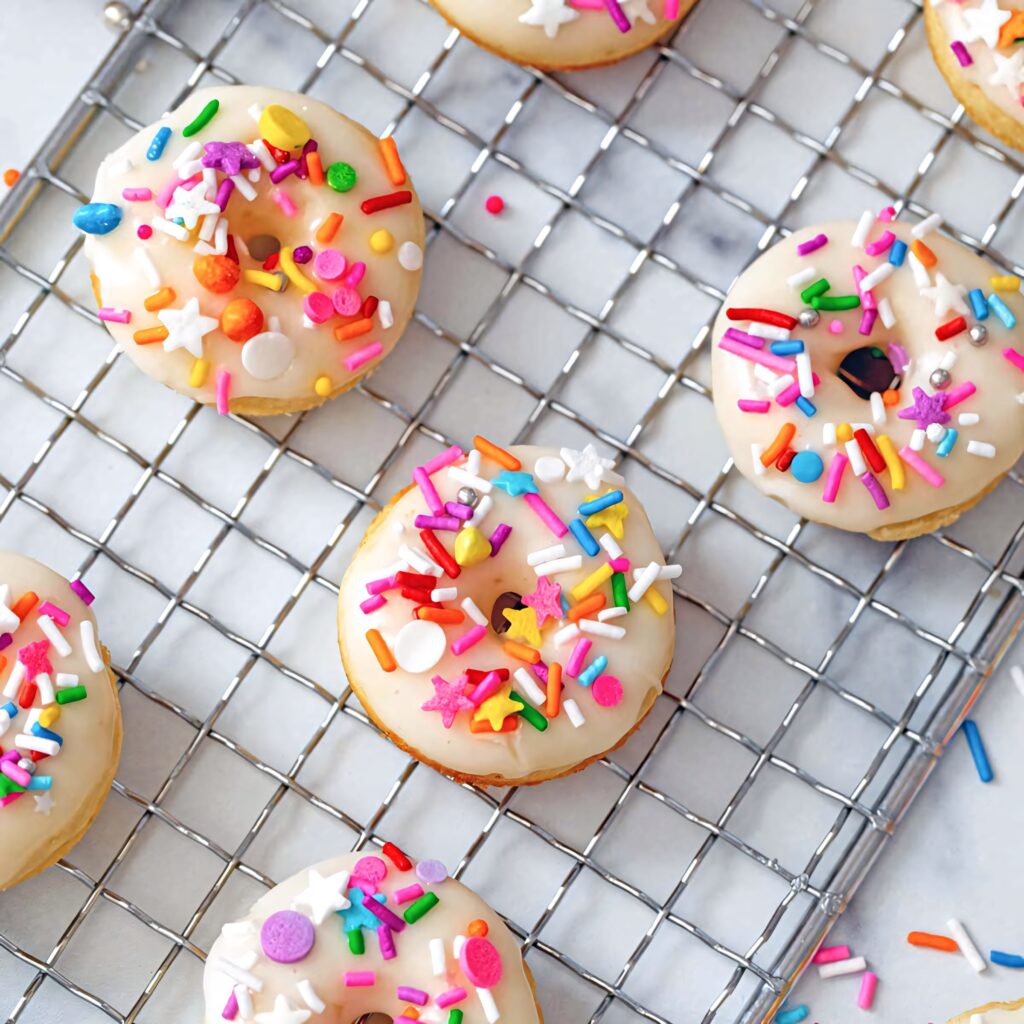 Colorful mini donuts with white icing and sprinkles on cooling rack marble background wallpaper