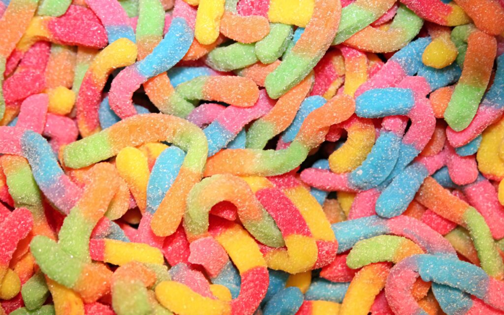 Colorful pastel gummy worm candies wallpaper with wavy shapes and soft sugary coating background