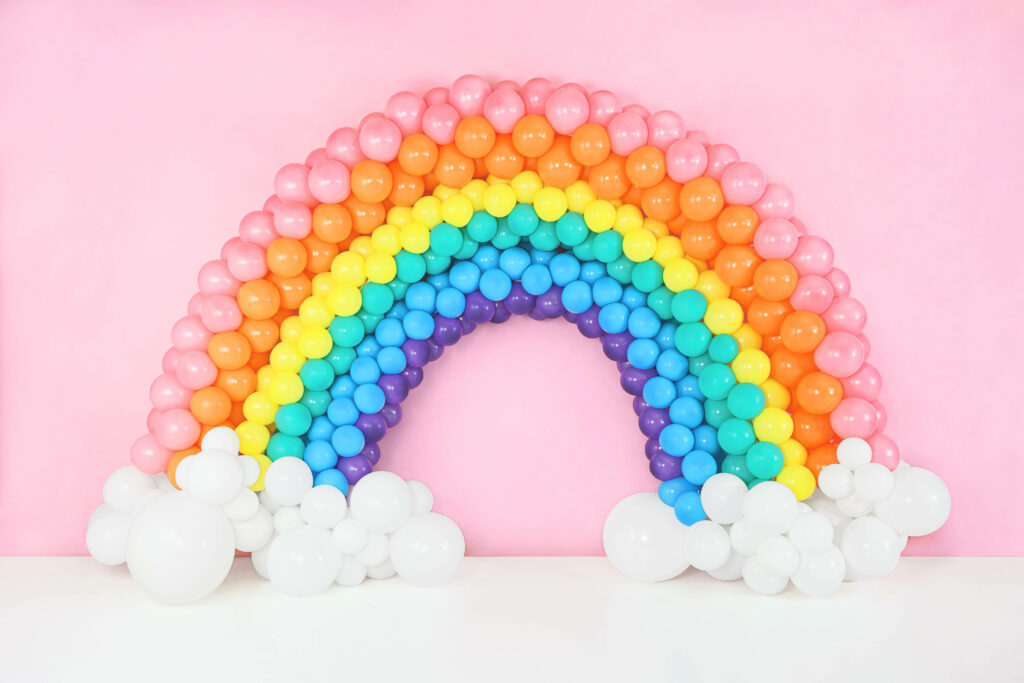 Colorful rainbow balloon arch with white cloud balloons on soft pink wallpaper background
