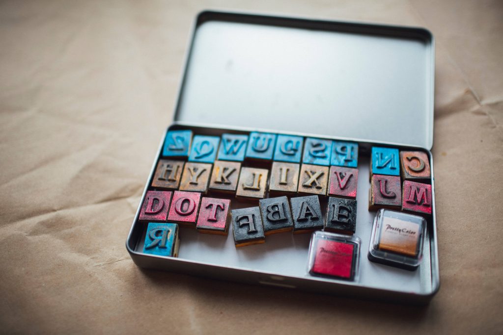 Metal tin box with colorful rubber letter stamps and ink pads on rustic craft paper background Wallpaper