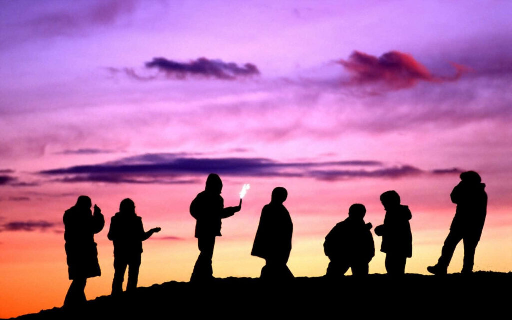 Friends celebrating with sparkler on ridge at twilight sky vibrant purple and orange background Wallpaper
