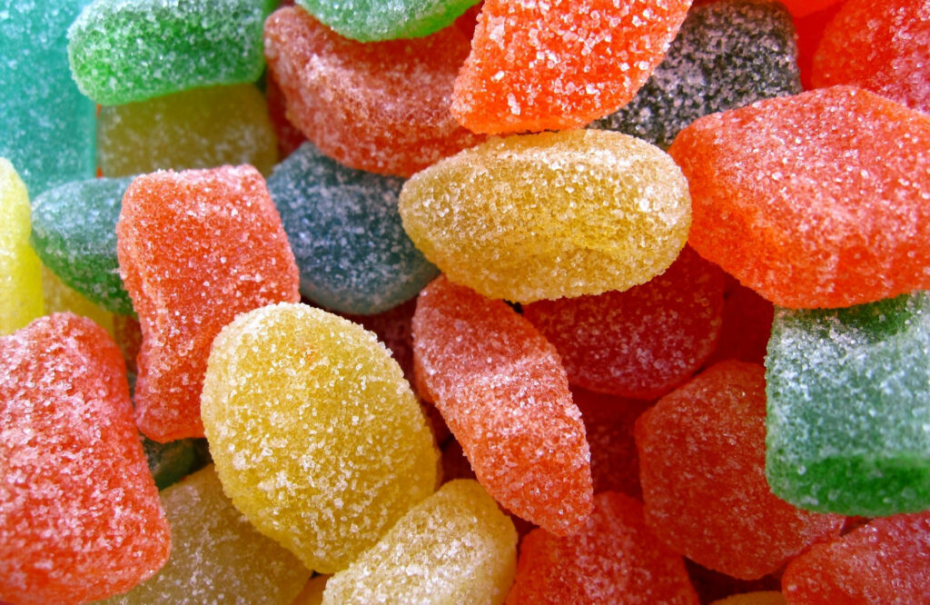 Close-up of colorful soft fruit jelly candies coated in sparkling sugar textured wallpaper background
