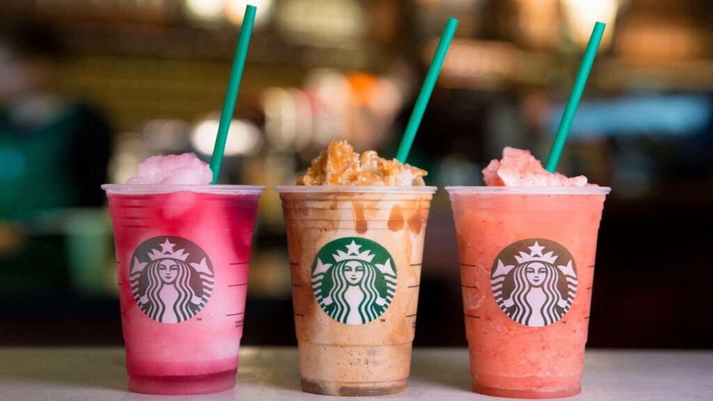 Three colorful Starbucks frappe drinks with green straws vibrant refreshing wallpaper background