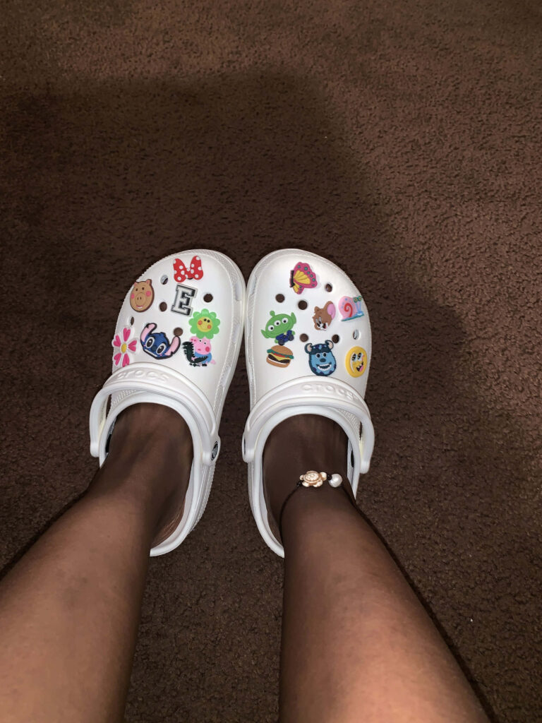 White Crocs decorated with colorful cartoon character and emoji stickers on brown carpet Wallpaper