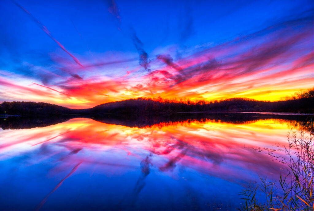 Colorful sunset wallpaper over calm river with orange pink and blue hues reflecting on water