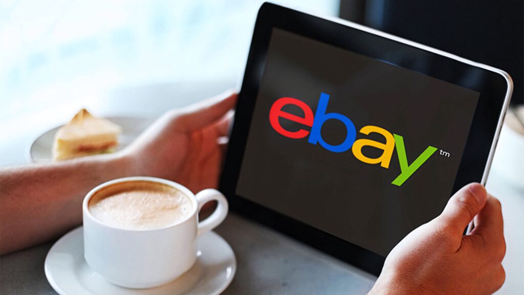 Person holding tablet showing colorful eBay logo with coffee cup and sandwich background cozy setting Wallpaper