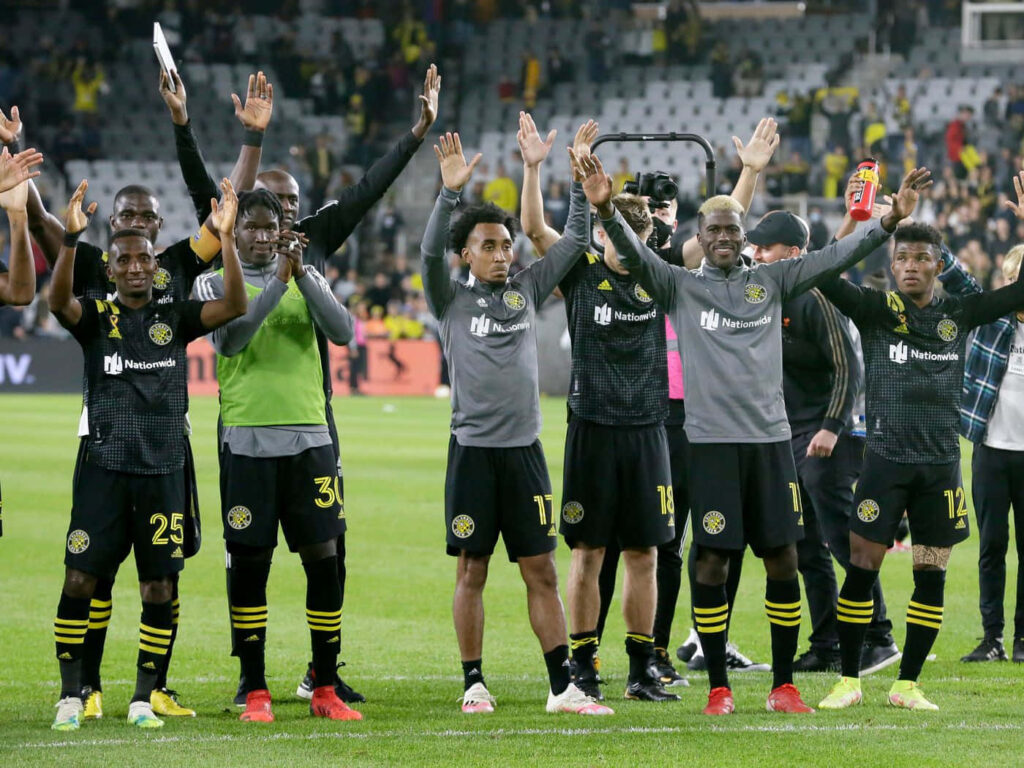 Columbus Crew soccer team celebrating on field in black and yellow uniforms stadium backdrop wallpaper