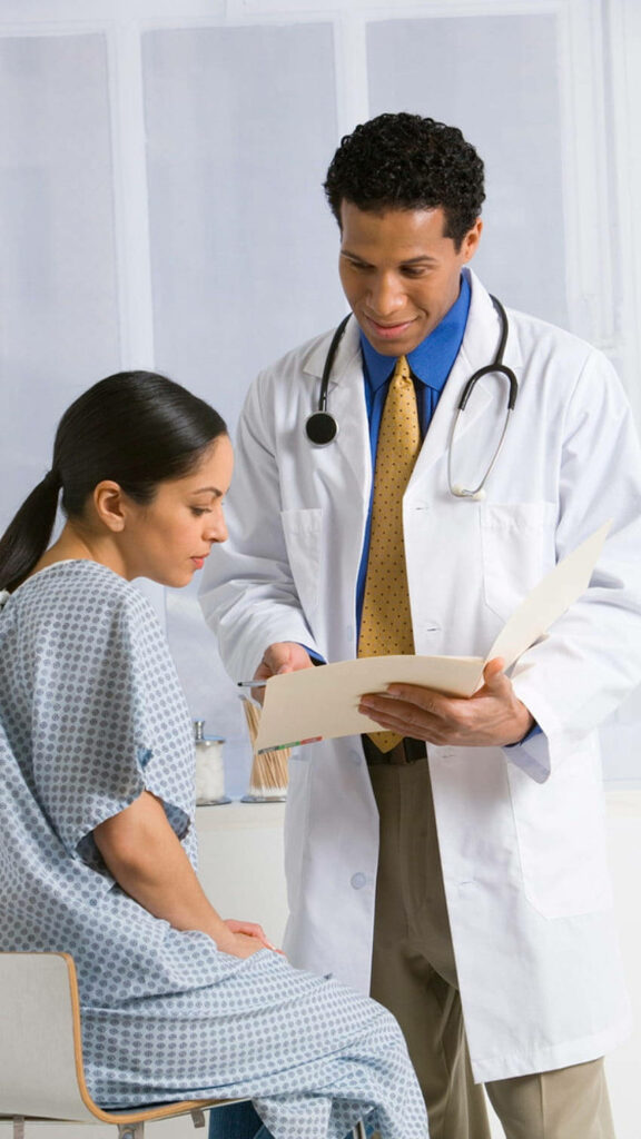 Caring doctor in white coat reviews medical notes with patient in hospital gown in clinic Wallpaper