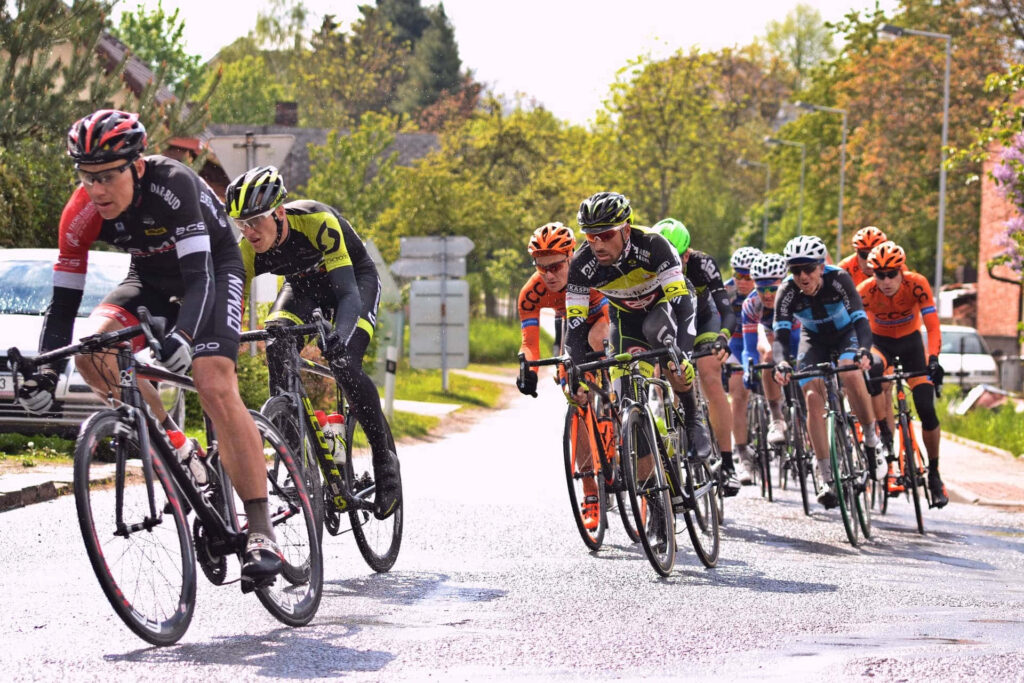 Competitive cyclists racing on a sunlit suburban street with vibrant jerseys and sleek bikes Wallpaper