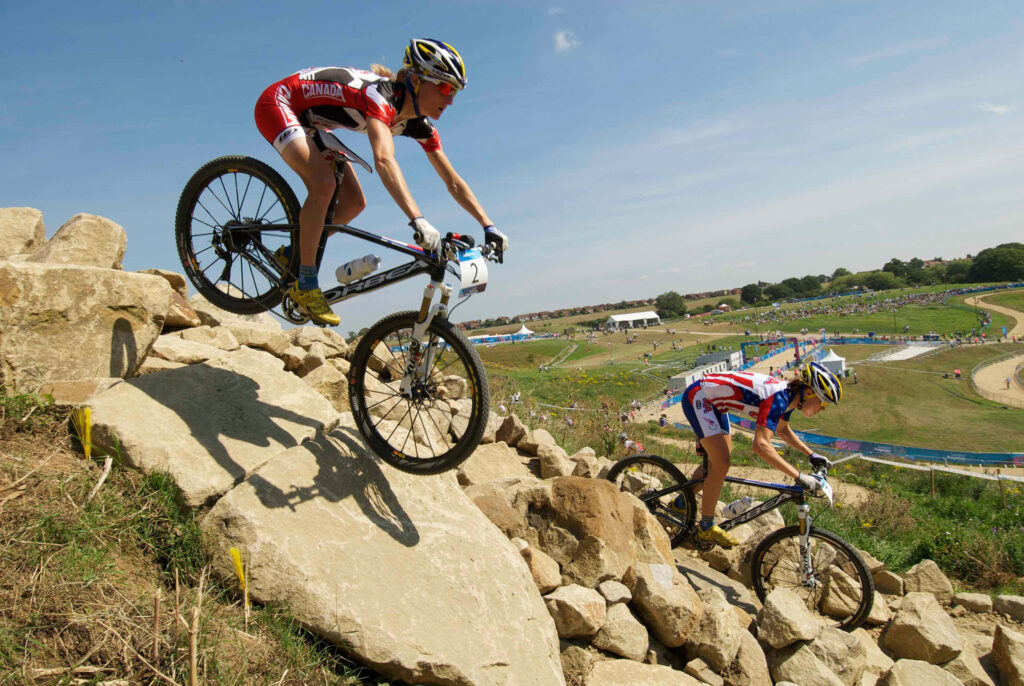 Two competitive cyclists ride rocky terrain under clear sky displaying action and adventure cycling Wallpaper