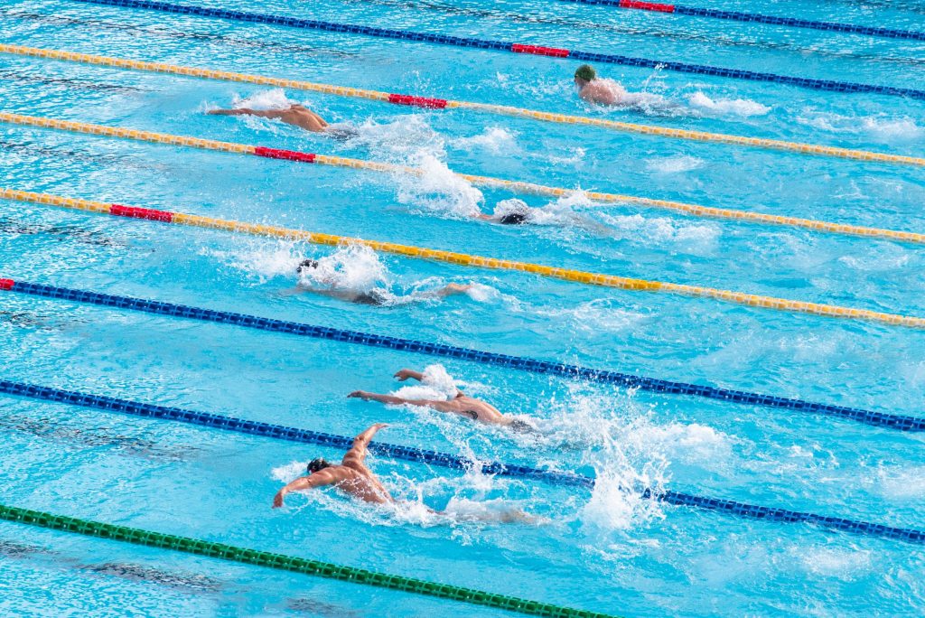 Competitive swimmers racing in bright blue pool water with dynamic splashes high-angle view Wallpaper