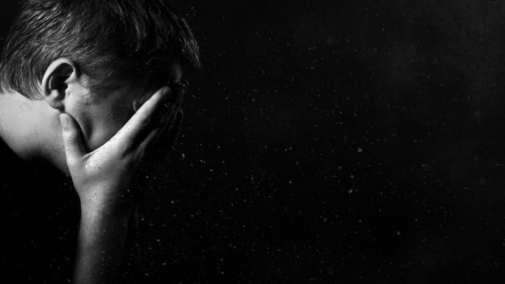 Black and white wallpaper of a man in profile hiding his face with hands showing grief and isolation