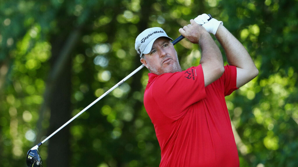 Concerned Boo Weekley mid-swing in red shirt and Taylormade cap on lush green golf course Wallpaper