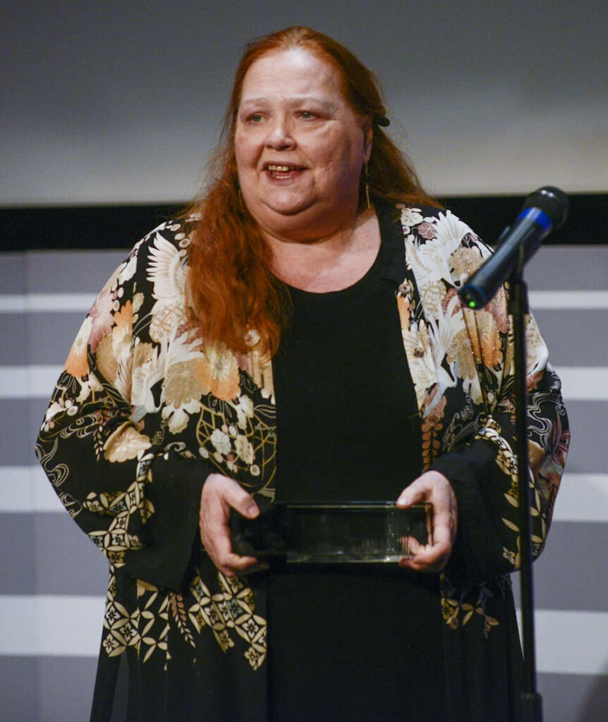 Conchata Ferrell confidently speaking on stage holding award wearing patterned kimono black dress Wallpaper
