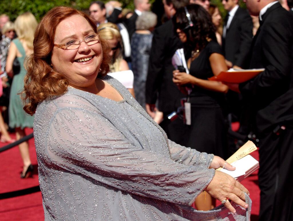 Conchata Ferrell in silver gown smiling on red carpet with lively glamorous event background Wallpaper