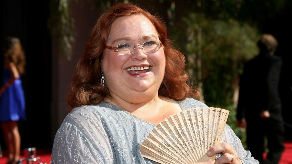 Conchata Ferrell smiling outdoors in light blue outfit holding decorative fan bright cheerful wallpaper
