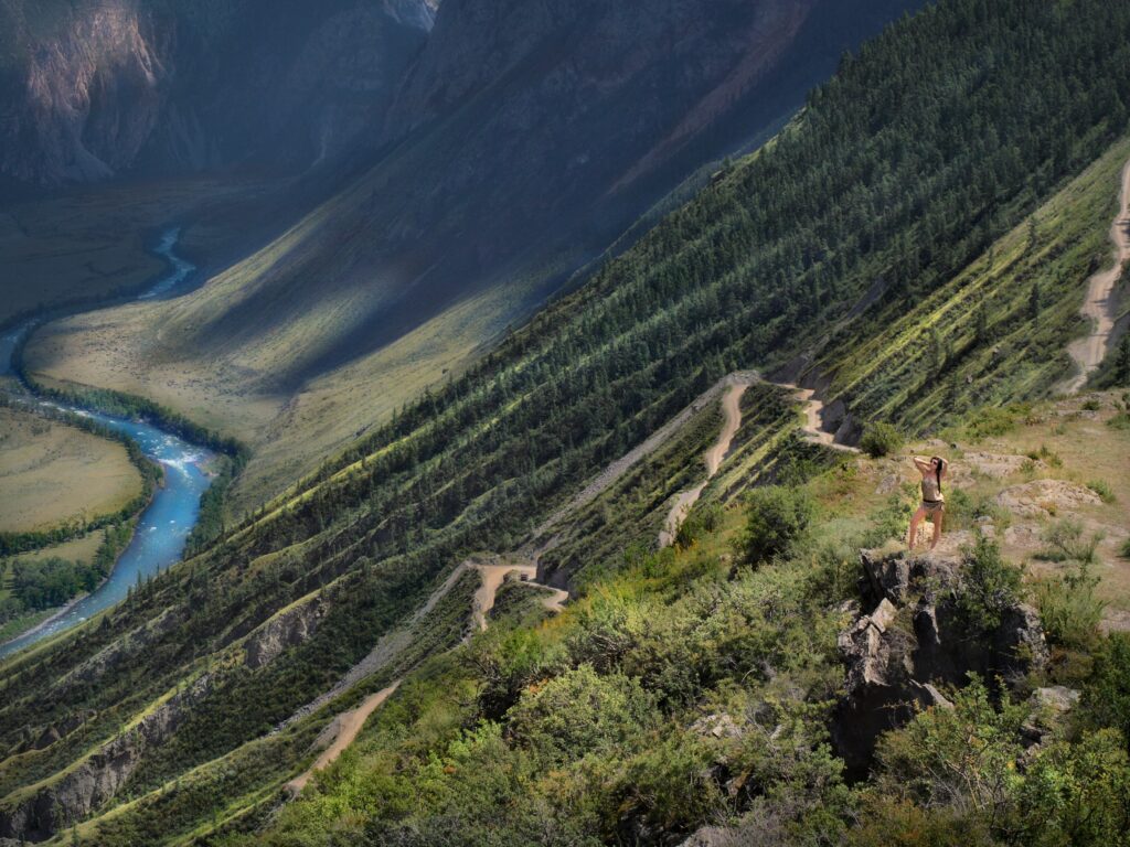 Confident girl on rugged mountain slope overlooking winding path and serene river landscape wallpaper
