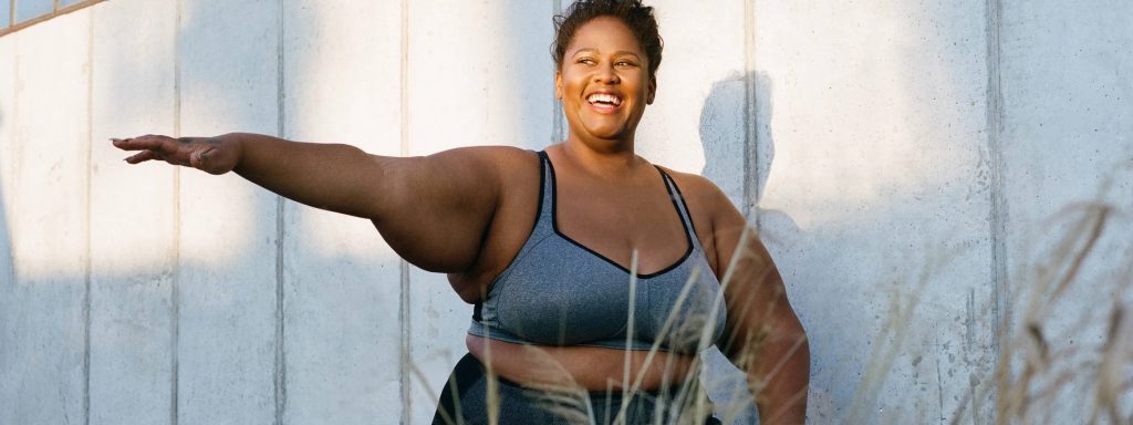 Joyful plus-size Black woman exercising outdoors smiling confidently in natural sunlight Wallpaper