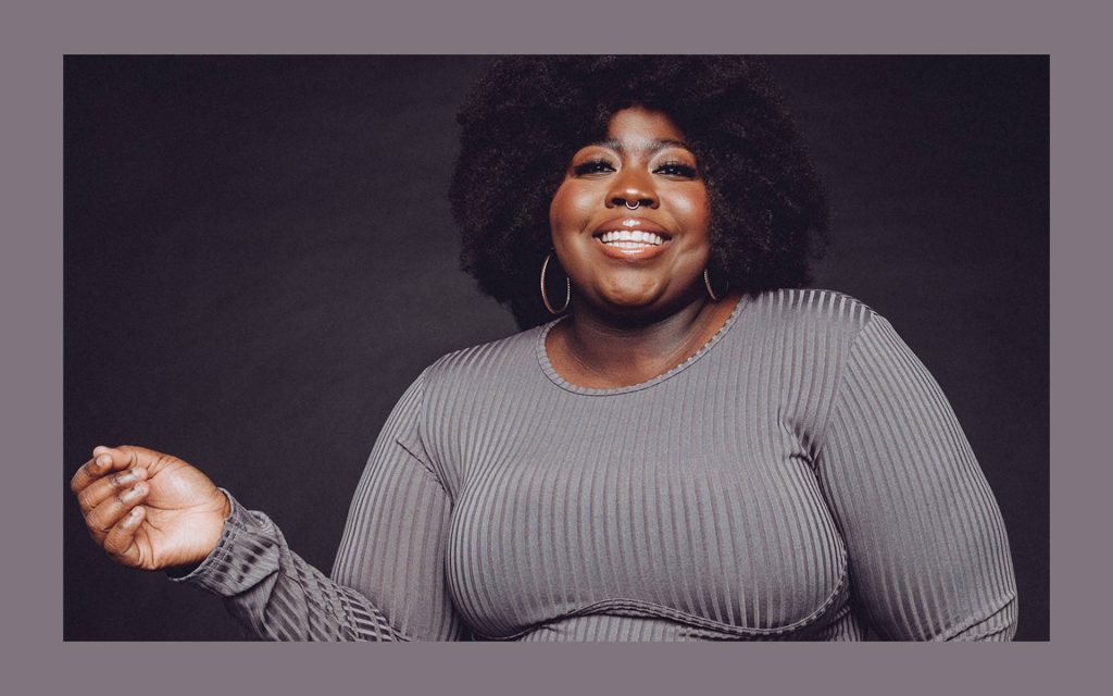 Confident plus size Black woman with natural afro smiling in gray top and hoop earrings studio portrait Wallpaper