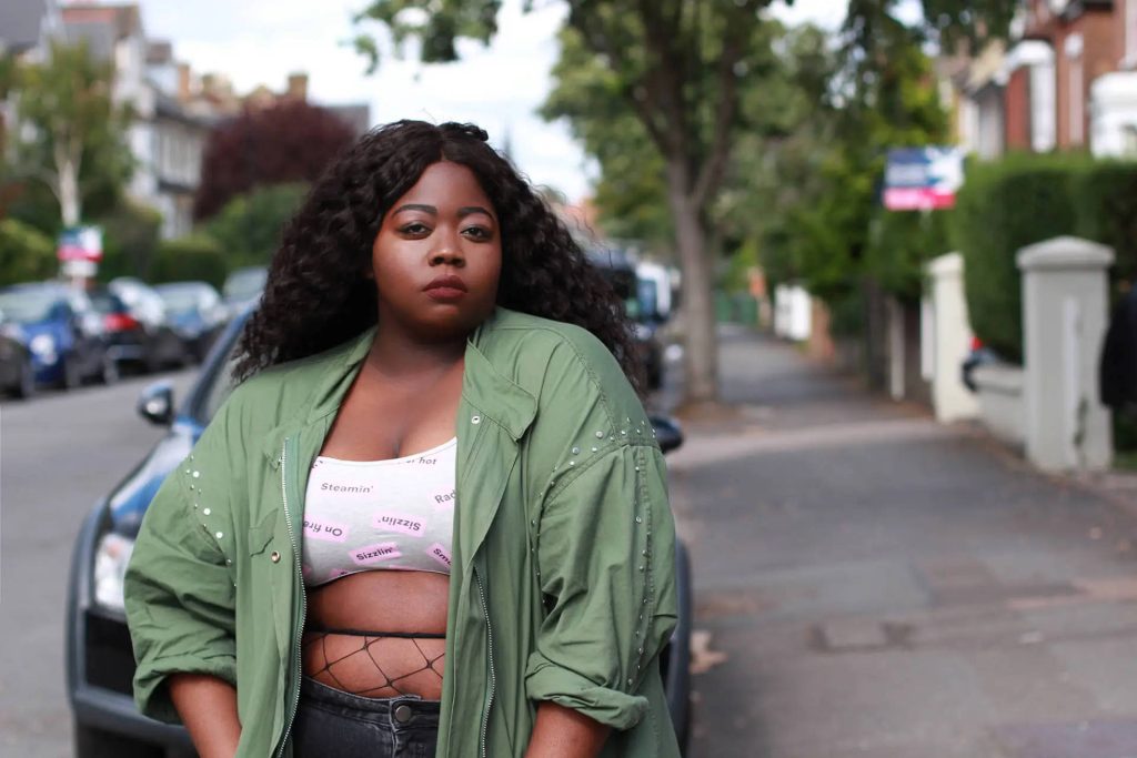 Plus-size Black woman with voluminous curls in olive jacket white crop top street style look Wallpaper