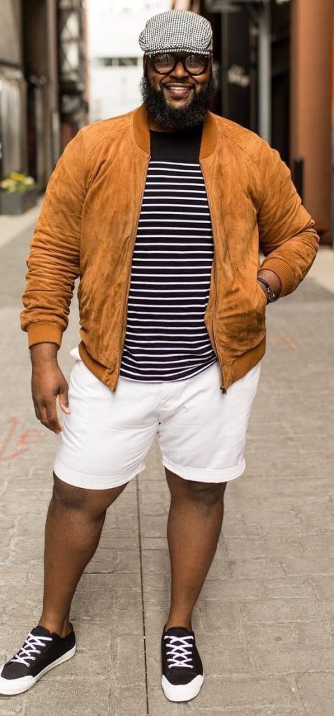 Plus-size man in tan bomber jacket white shorts black sneakers flat cap urban street style portrait Wallpaper