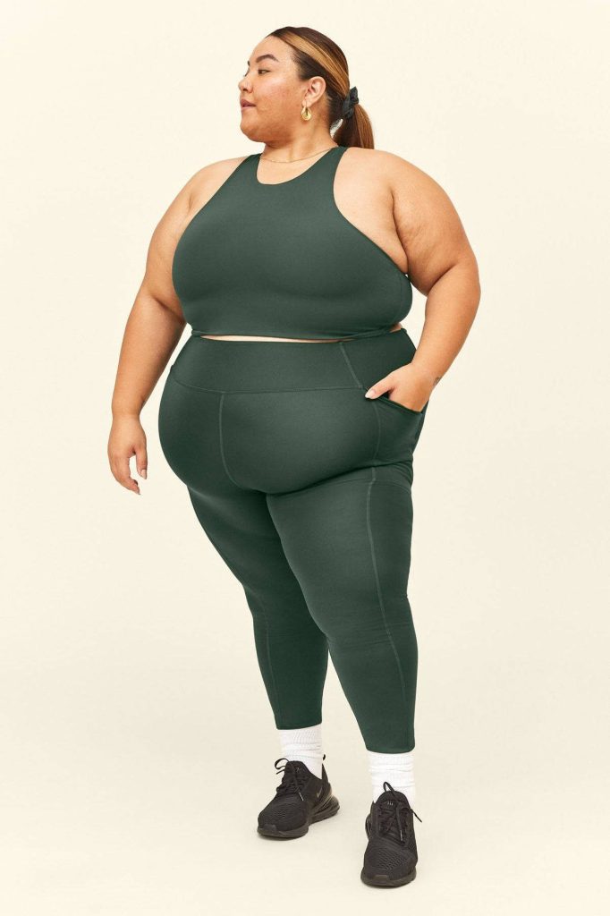 Plus-size woman in forest green workout set with sneakers on cream background active pose Wallpaper