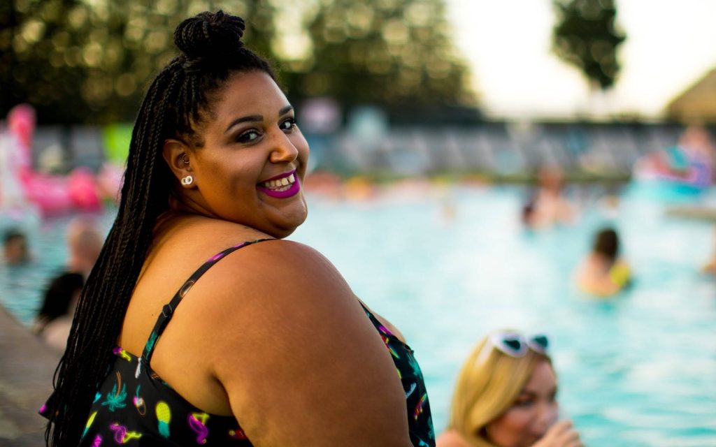 Plus-size woman in neon swimsuit smiling poolside in natural light summer resort wallpaper background