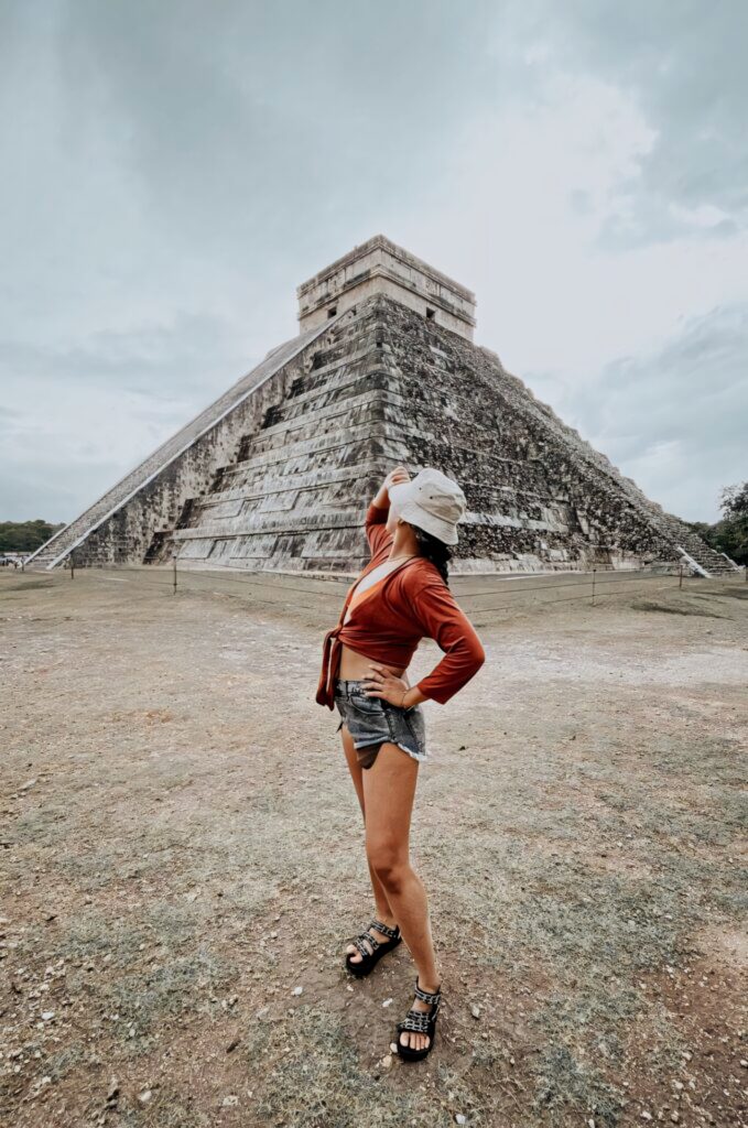 Confident woman posing at Chichen Itza pyramid under dramatic cloudy sky with ancient stone textures Wallpaper