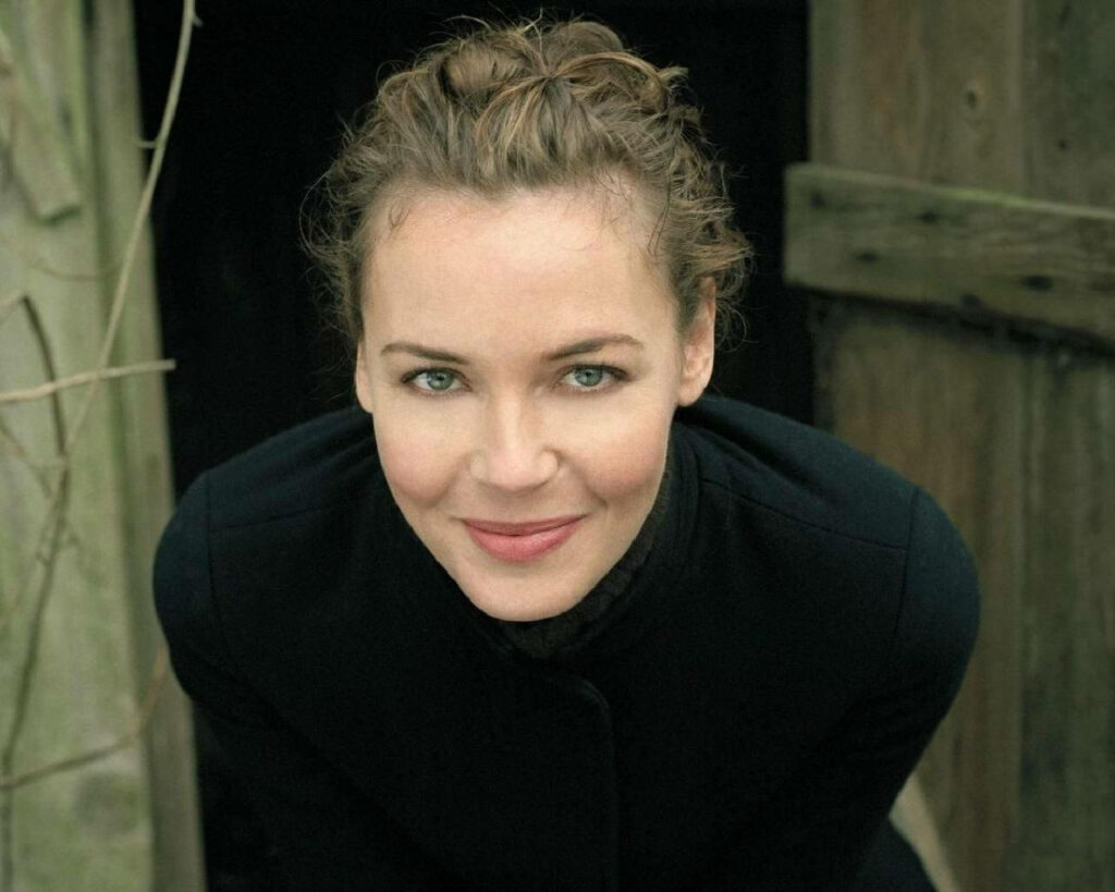 Connie Nielsen close-up portrait warm smile rustic wooden background soft natural lighting Wallpaper